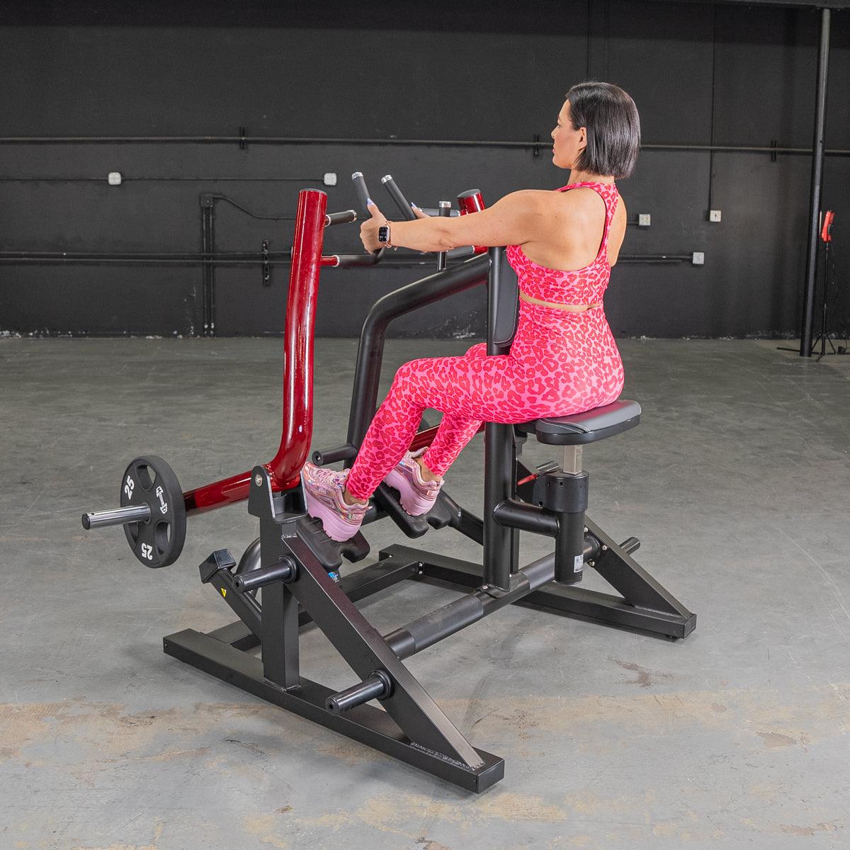 Woman in pink leopard print workout outfit using seated row machine in gym.
