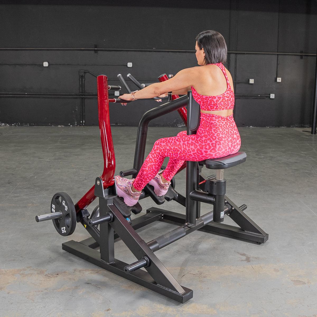 Woman in pink leopard print activewear using a seated row machine in a gym.
