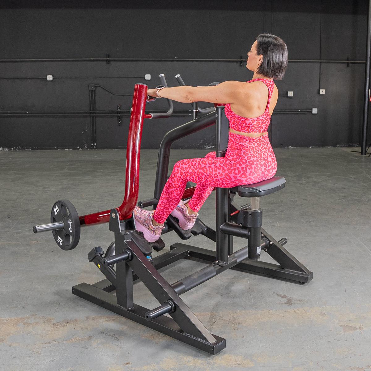 Woman in pink leopard print outfit using seated row machine at gym.