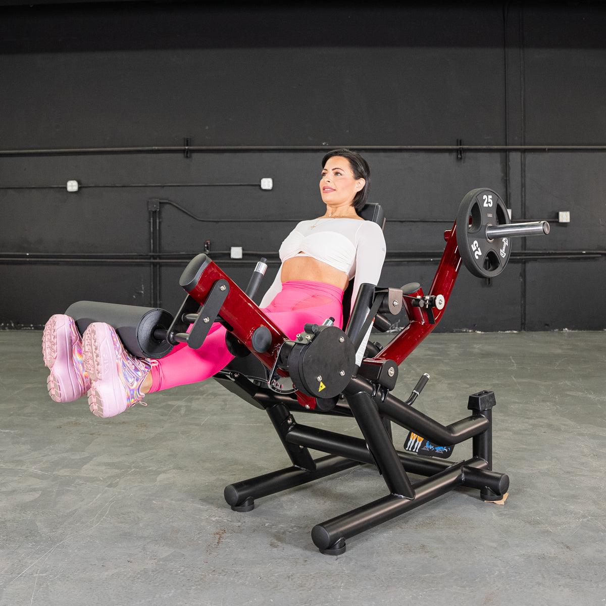 Woman on power-leverage leg extension/lying leg curl machine in a gym.
