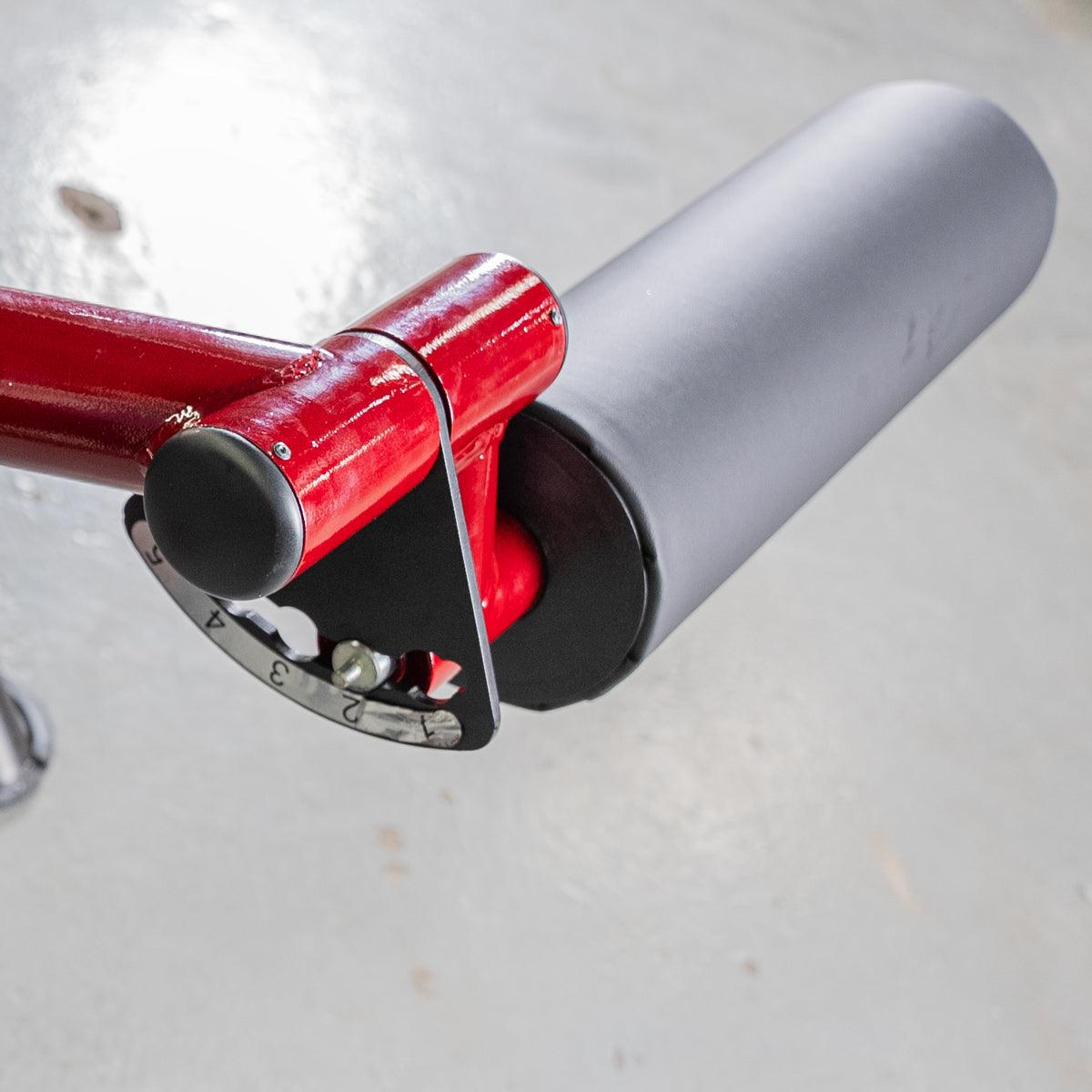 Close-up of a red Power Leverage Prone Leg Curl machine with gray roller pad.
