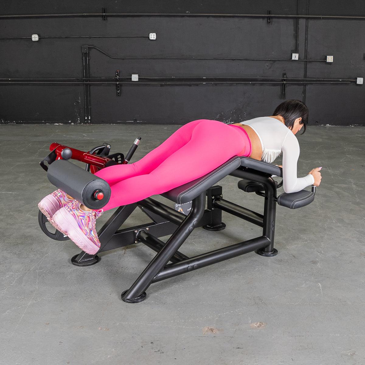 Woman in pink leggings on a prone leg curl bench at gym.