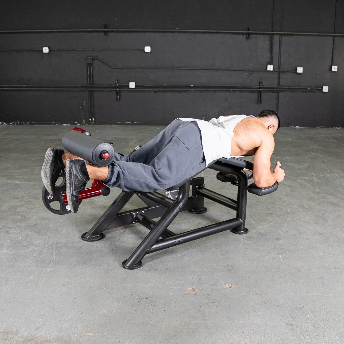 Man using a prone leg curl machine on a bench at the gym.