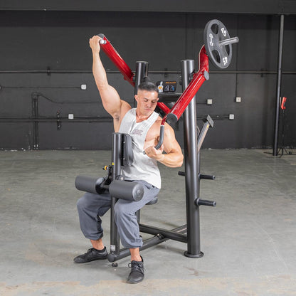 Man using red shoulder press machine in gym.
