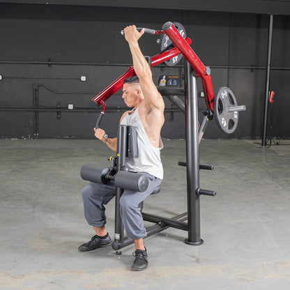 Man using red seated shoulder press machine in gym.