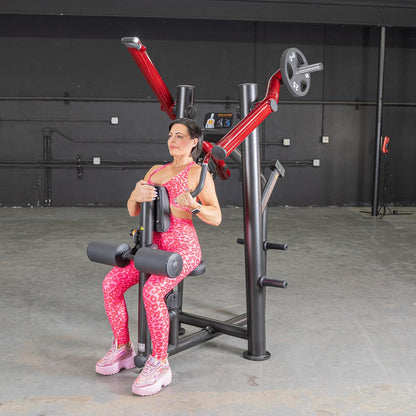 Woman using a red and black shoulder press machine in a gym, wearing a pink leopard print workout outfit.