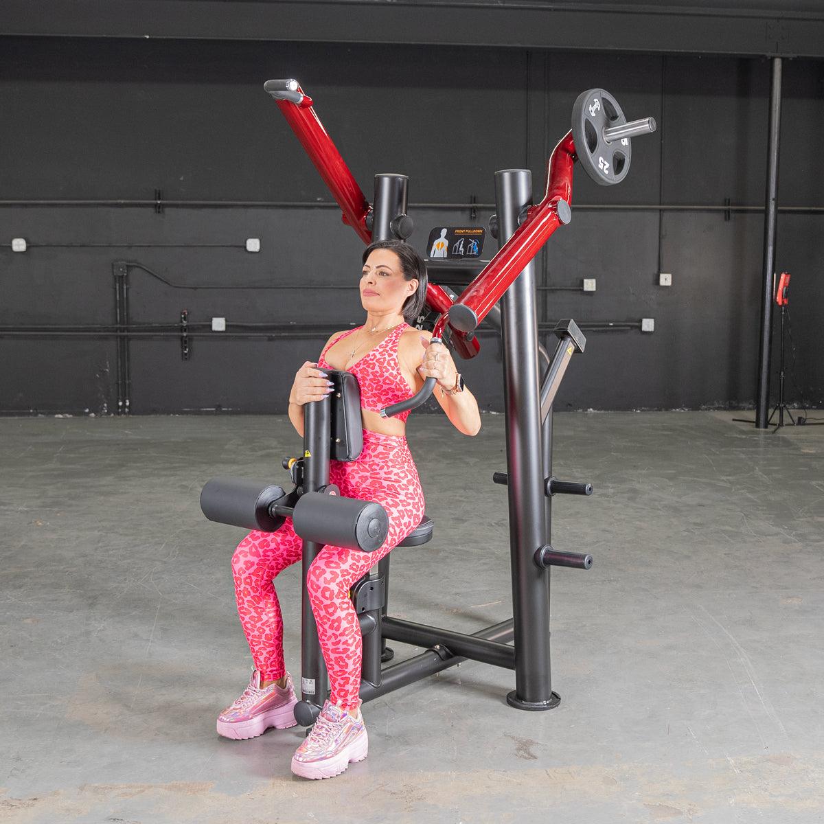 Woman in pink leopard workout set using a red chest press machine in gym.