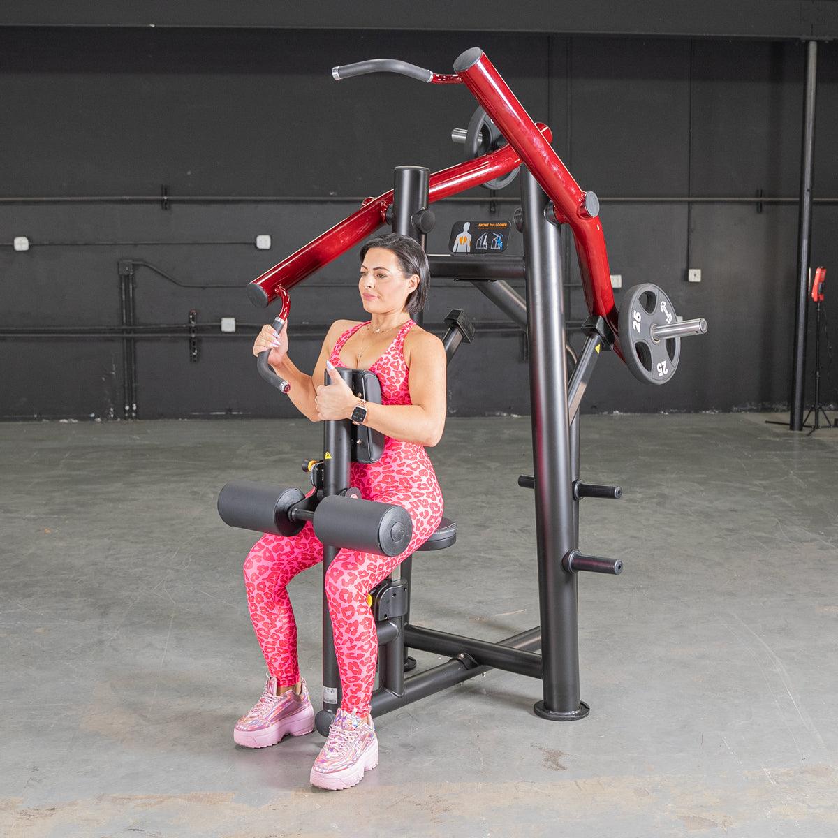 Woman using red and black chest press machine in gym, wearing pink leopard print workout outfit.