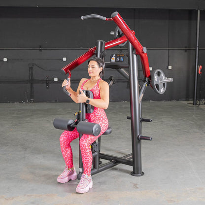 Woman using red and black chest press machine in gym, wearing pink leopard print workout outfit.