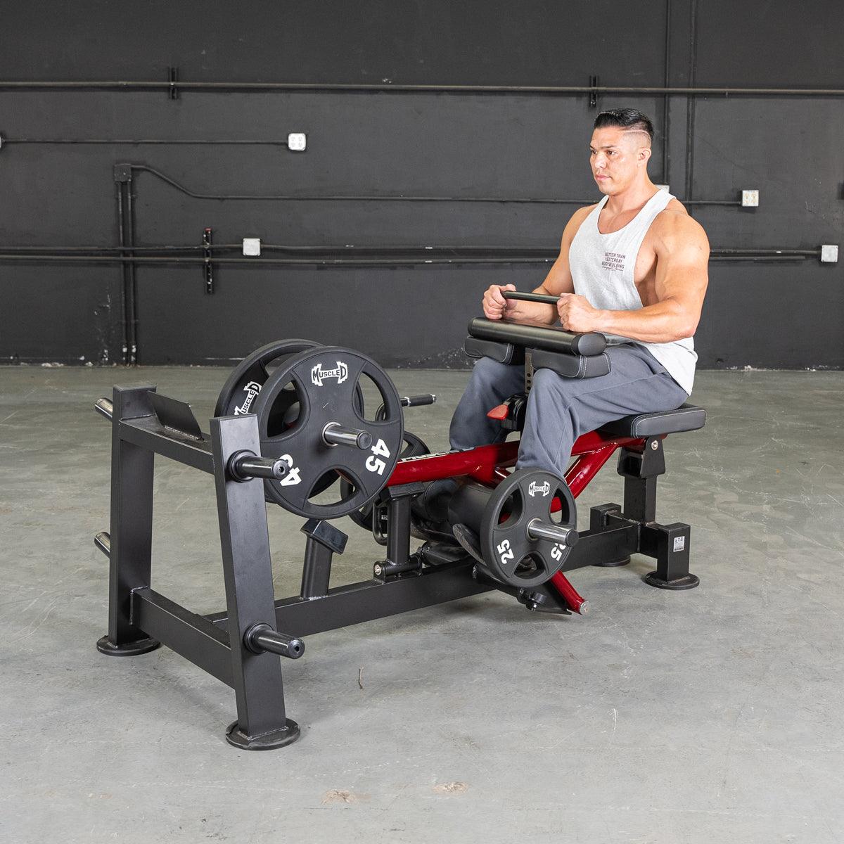 Man sits on a power-leverage leg machine with weights in a gym.