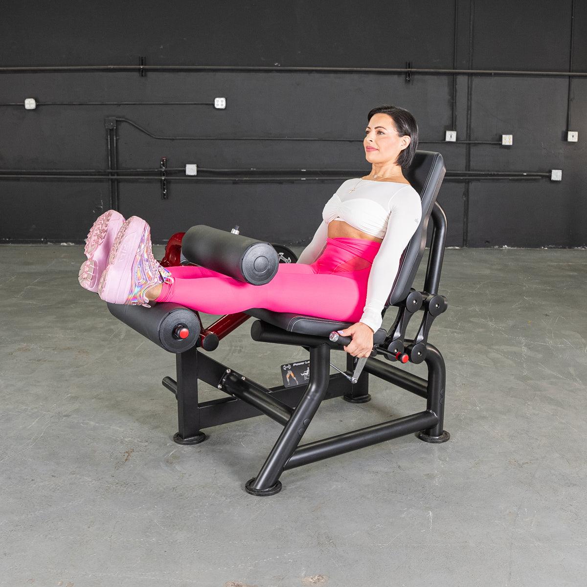 Woman in bright pink leggings using a seated leg curl machine at the gym.