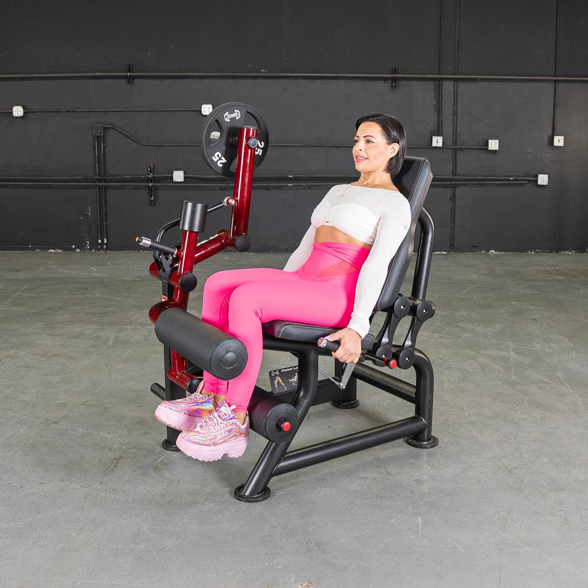 Woman seated on leg curl machine in gym wearing pink leggings