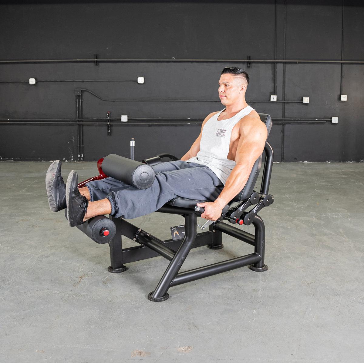 Man seated on Power-Leverage V2 leg curl machine at gym.