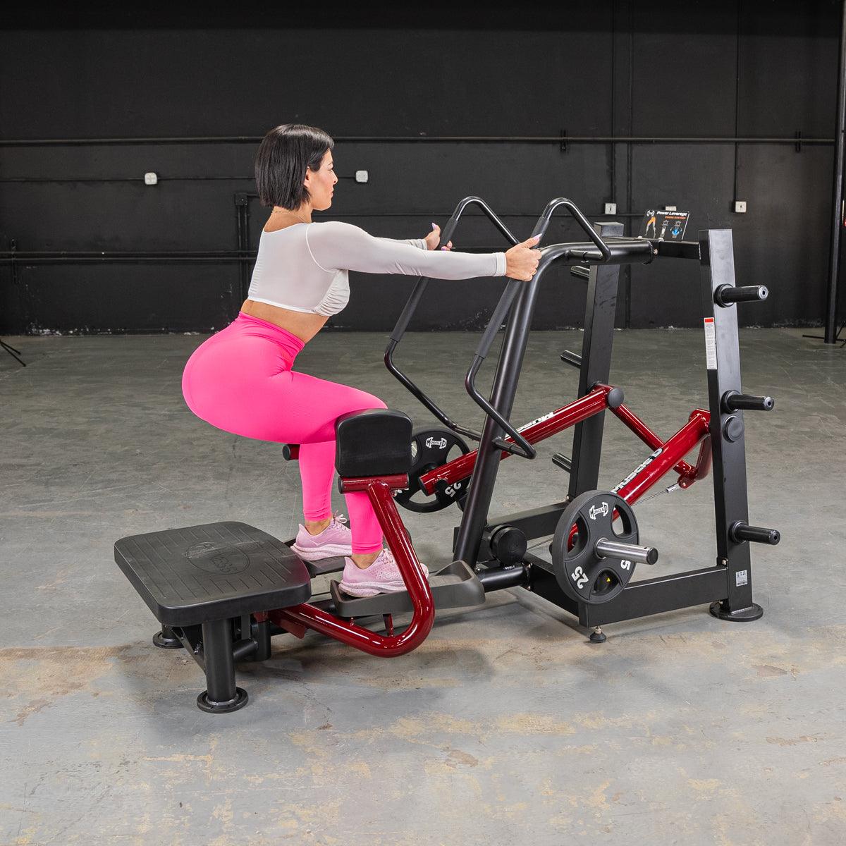 Woman in pink leggings uses standing hip abductor machine.