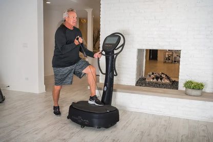 Man performing a dynamic exercise on a black Power Plate vibration platform with digital display, in a modern home gym with white brick walls.