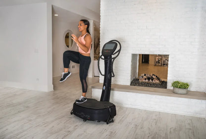 Woman performing a high knee exercise on a black Power Plate vibration platform in a modern home gym with white brick walls.