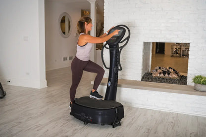 Woman performing a squat on a black Power Plate vibration platform with digital display in a modern home gym setting.