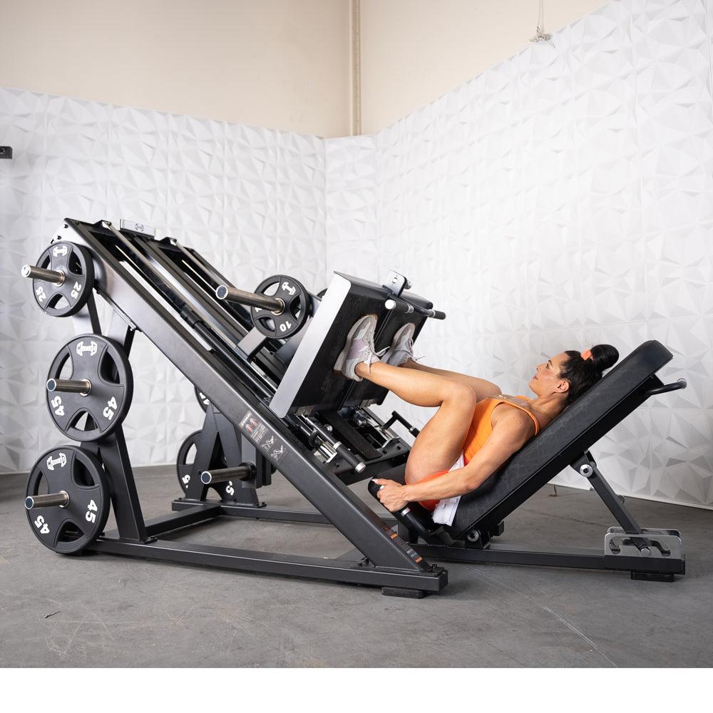 Woman performing leg press on a dual-leg press machine in gym.