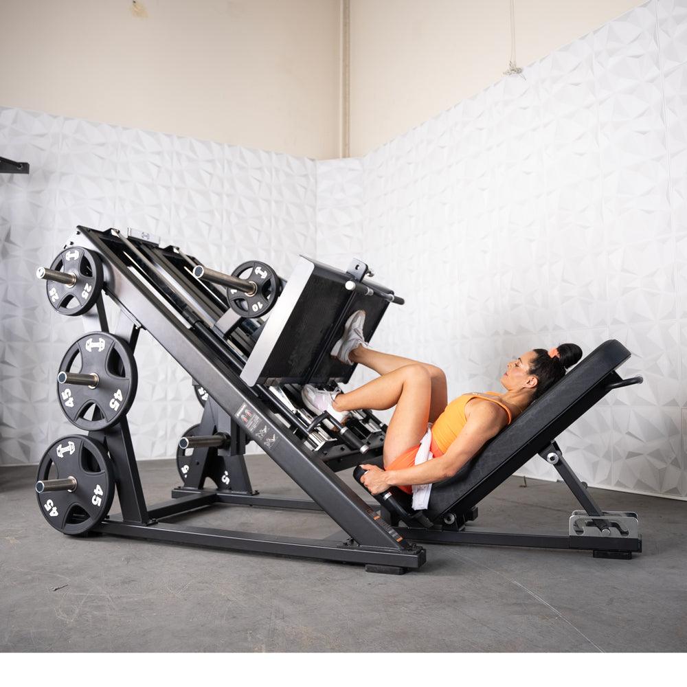 Woman in orange workout outfit using a leg press machine in gym.