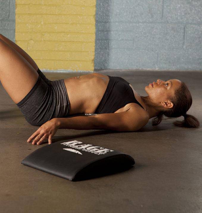 Person lying on a mat with a black foam roller underneath their leg, against a textured wall.