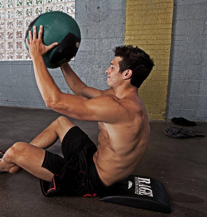Man exercising with a medicine ball against a brick wall.
