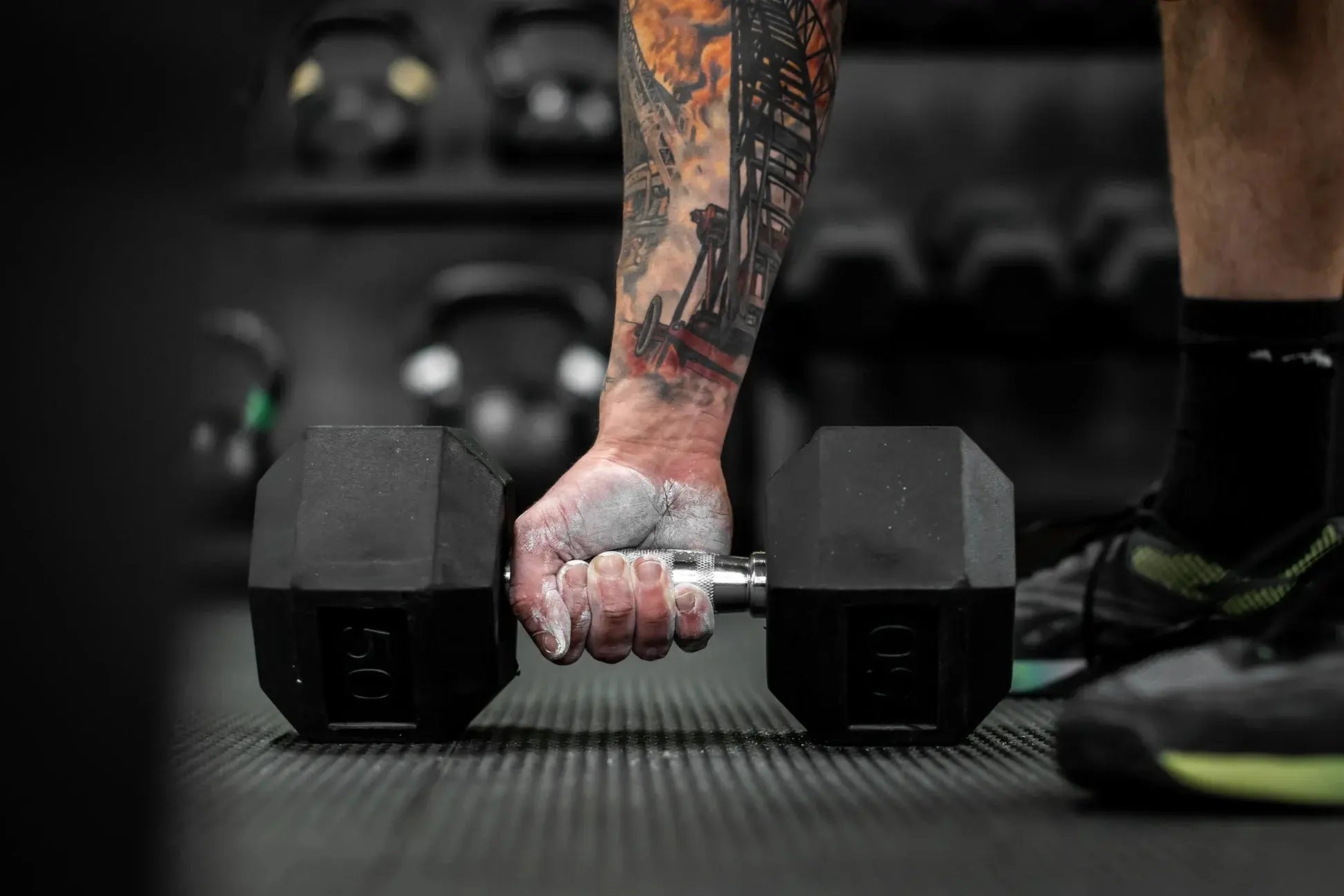Tattooed hand gripping a dumbbell with chalk powder.