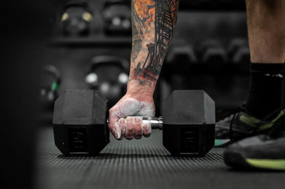 Tattooed hand gripping a dumbbell with chalk powder.