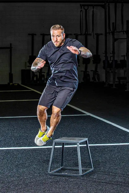 Man performing a jump over a small box in a gym setting