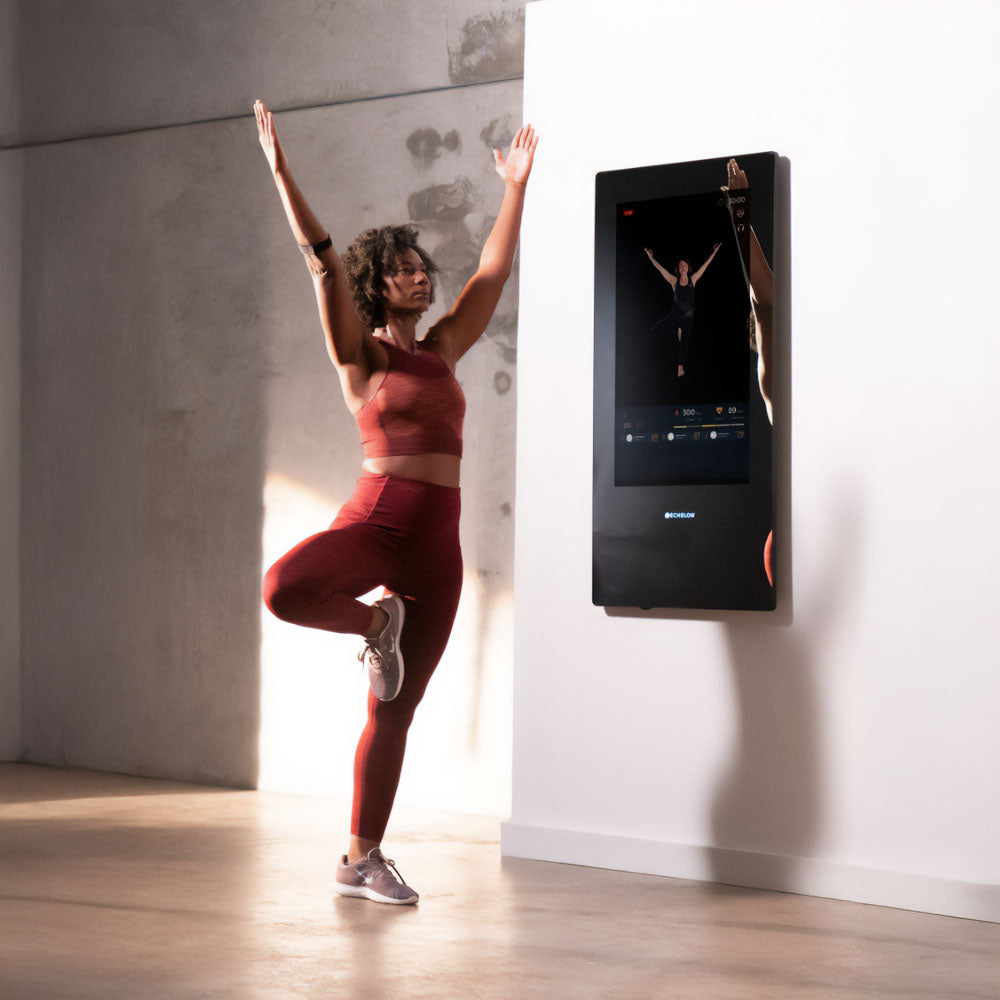 A person practicing yoga in front of an Echelon Reflect 50 Smart Fitness Mirror, showcasing a fitness routine in a modern, well-lit space.
