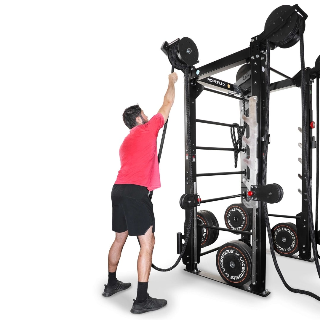 Man using Roperflex rope machine in gym, wearing red shirt and black shorts.