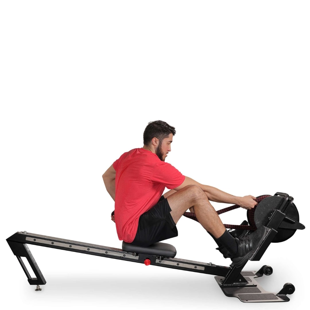 Man exercising on black rowing machine in red shirt and black shorts.