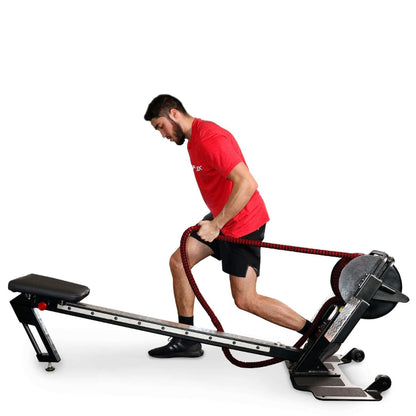 Man exercising on a SkiErg in a red shirt and black shorts, pulling a resistance rope.