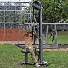 Soldier in camouflage using a rope climbing trainer outdoors for military fitness training.