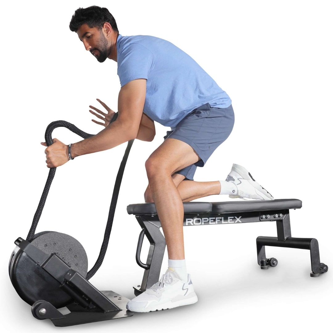 Man exercising with Ropeflex machine, kneeling on a bench, wearing blue shirt and shorts.