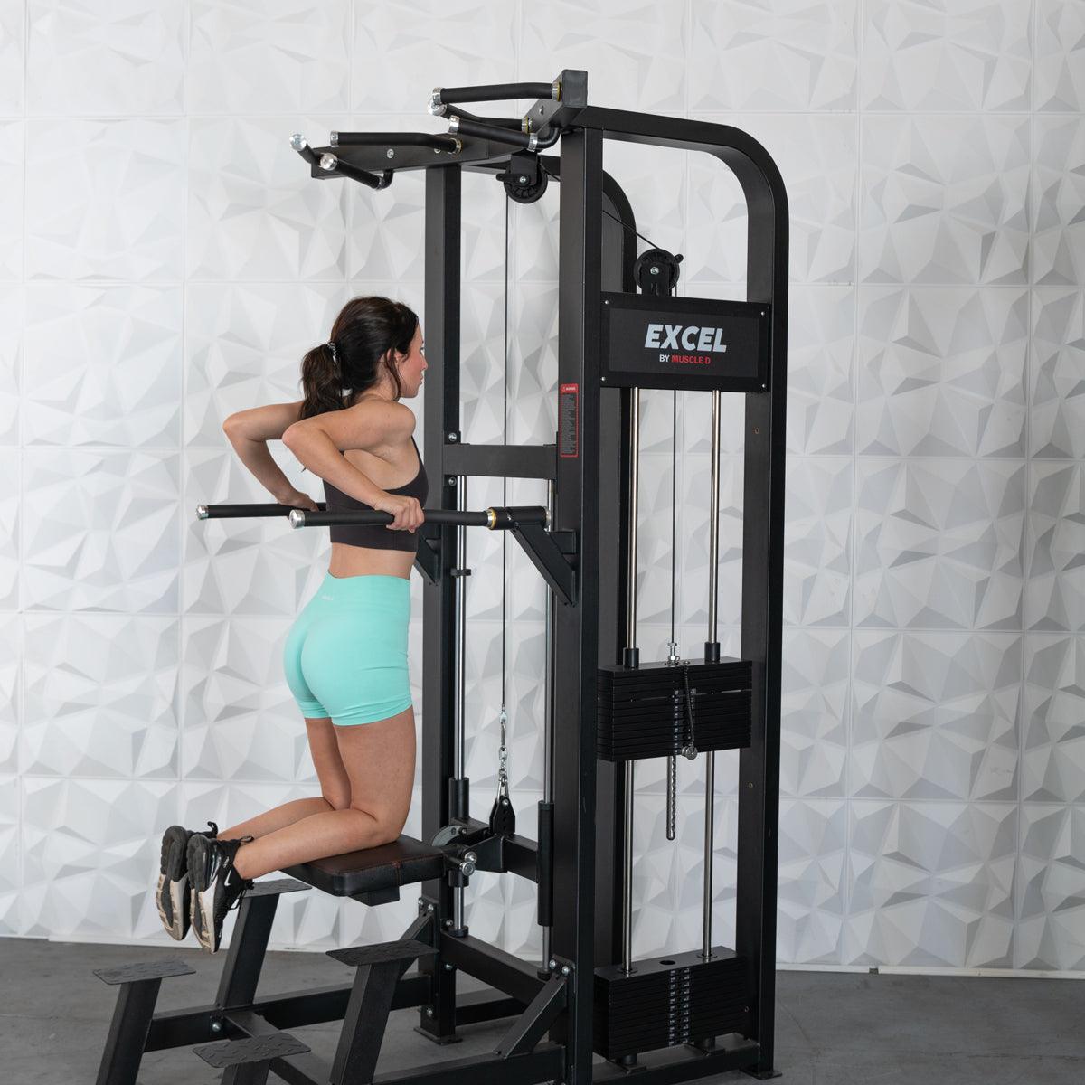Woman using Excel dip machine in gym, wearing mint shorts for strength training.