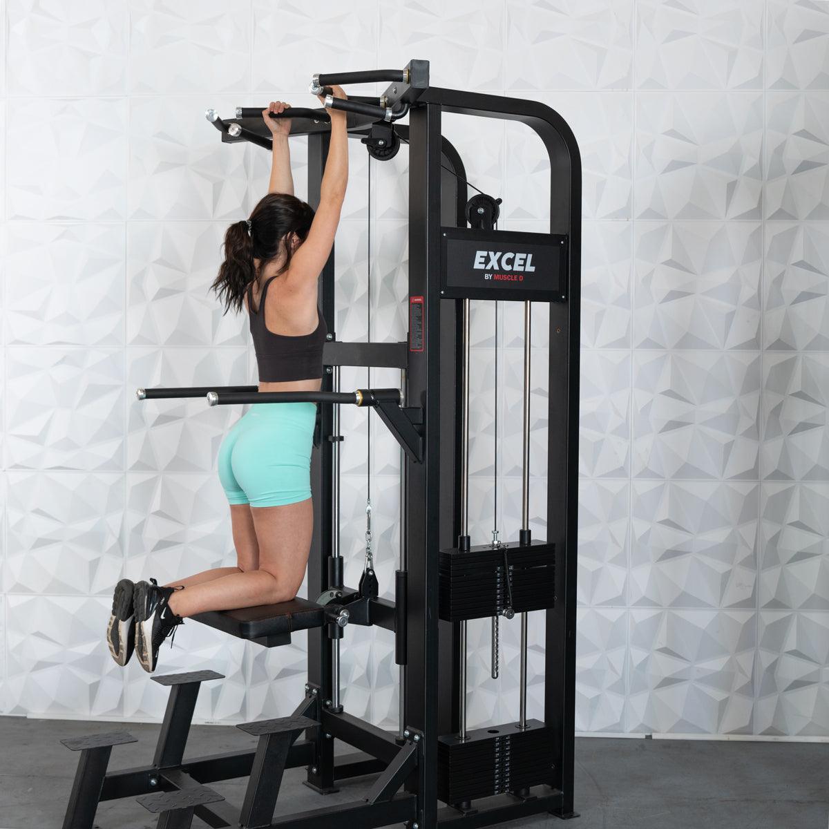 Woman using Excel pull-up machine in gym, wearing turquoise shorts.