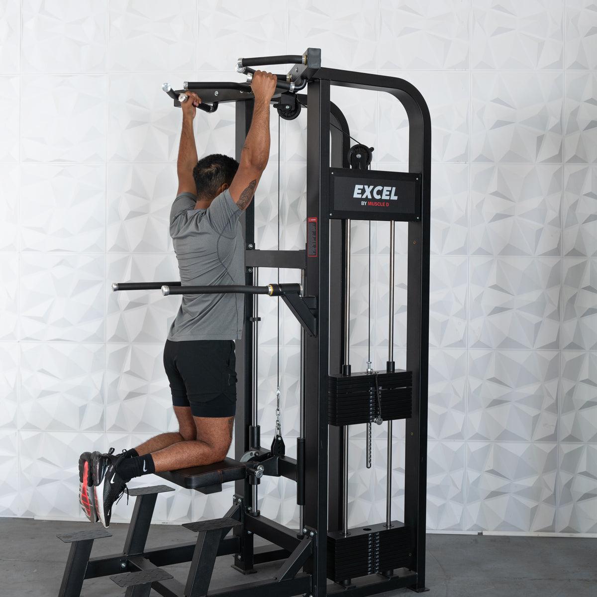 Man using Excel pull-up machine in gym wearing gray shirt and black shorts.