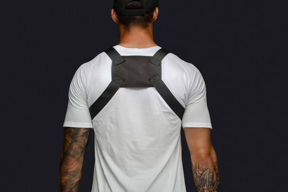 Back view of person in white T-shirt wearing a gray chest rig with cross-back straps.