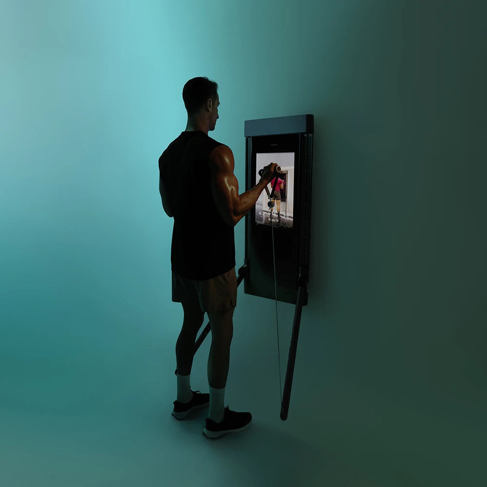 Man using a wall-mounted Tonal trainer in a teal-toned studio.