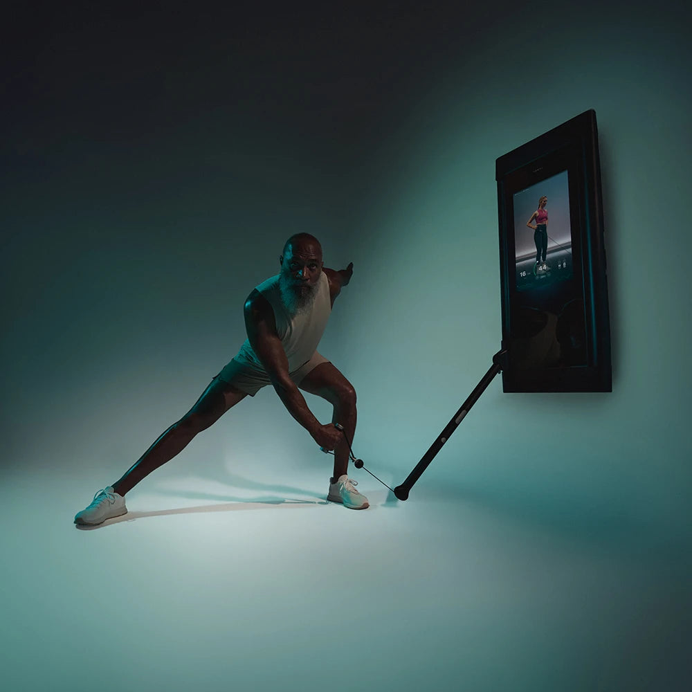 Elderly man exercising with a wall-mounted Tonal trainer and screen.