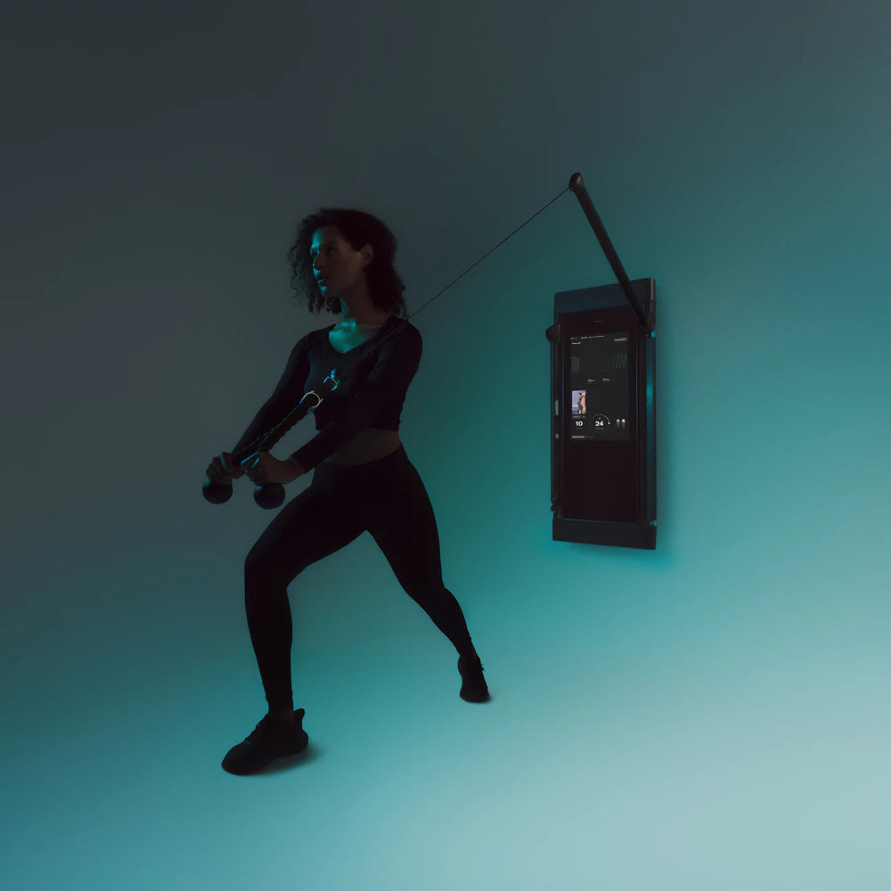 Woman training with a wall-mounted Tonal T800 Trainer Bundle in teal lighting.