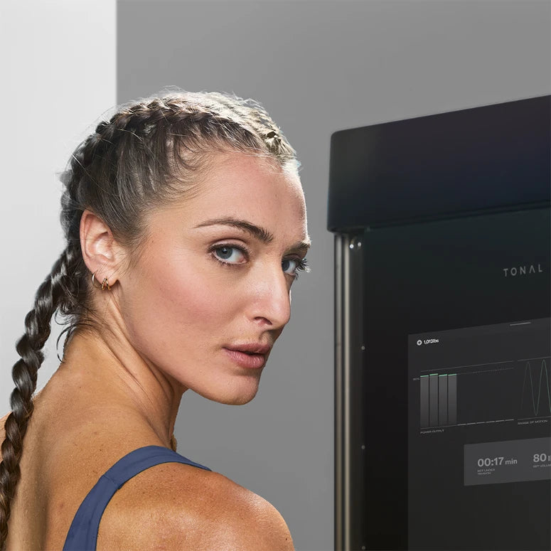 Athletic woman with braided hair beside a Tonal T800 trainer.