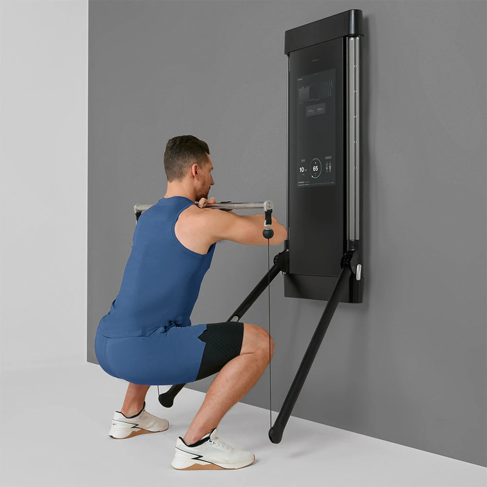 Man performing squat with wall-mounted Tonal trainer in home gym