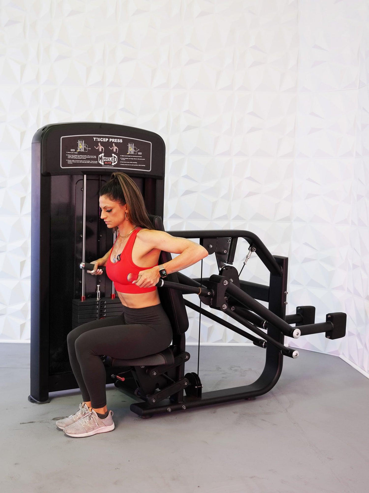 Woman seated on a triceps press machine performing an exercise in a gym.