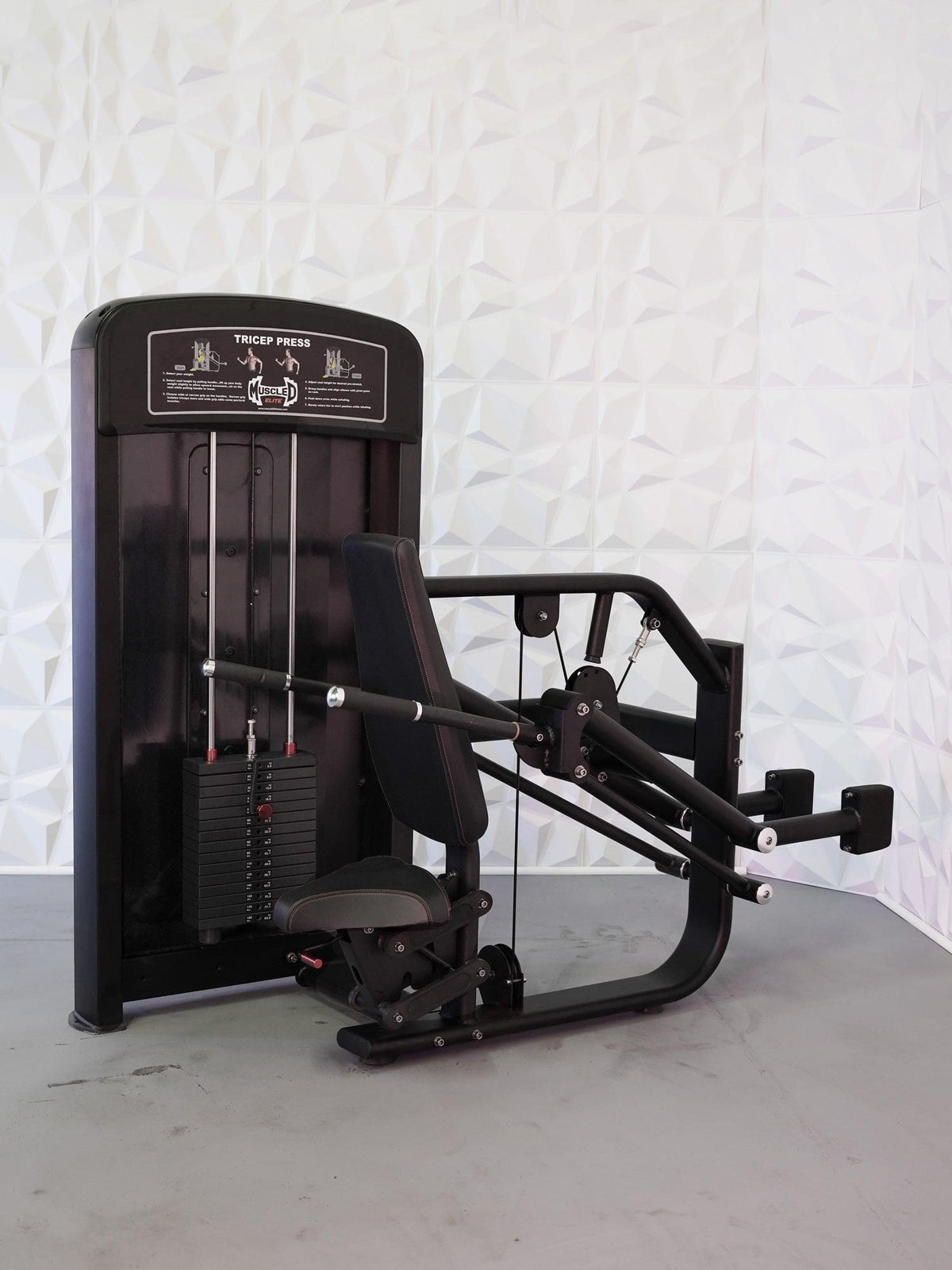 Black tricep press gym machine with weight stack and padded seat in a studio.