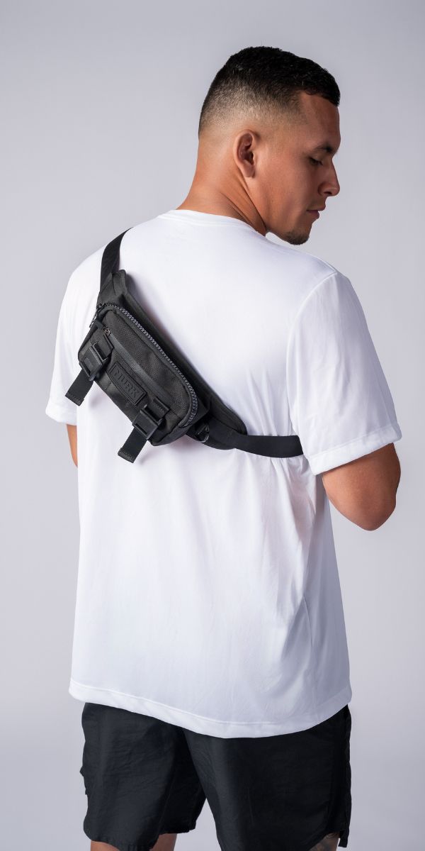 Man in a white t-shirt wearing a black crossbody sling bag across his chest/back.