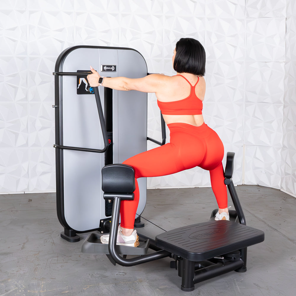 Woman in red athletic wear using a standing abductor machine at the gym.