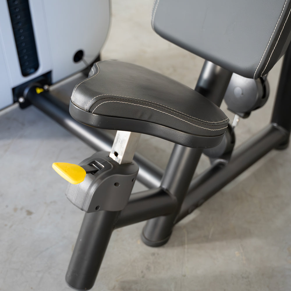 Padded seat of a triceps extension machine with yellow lever.