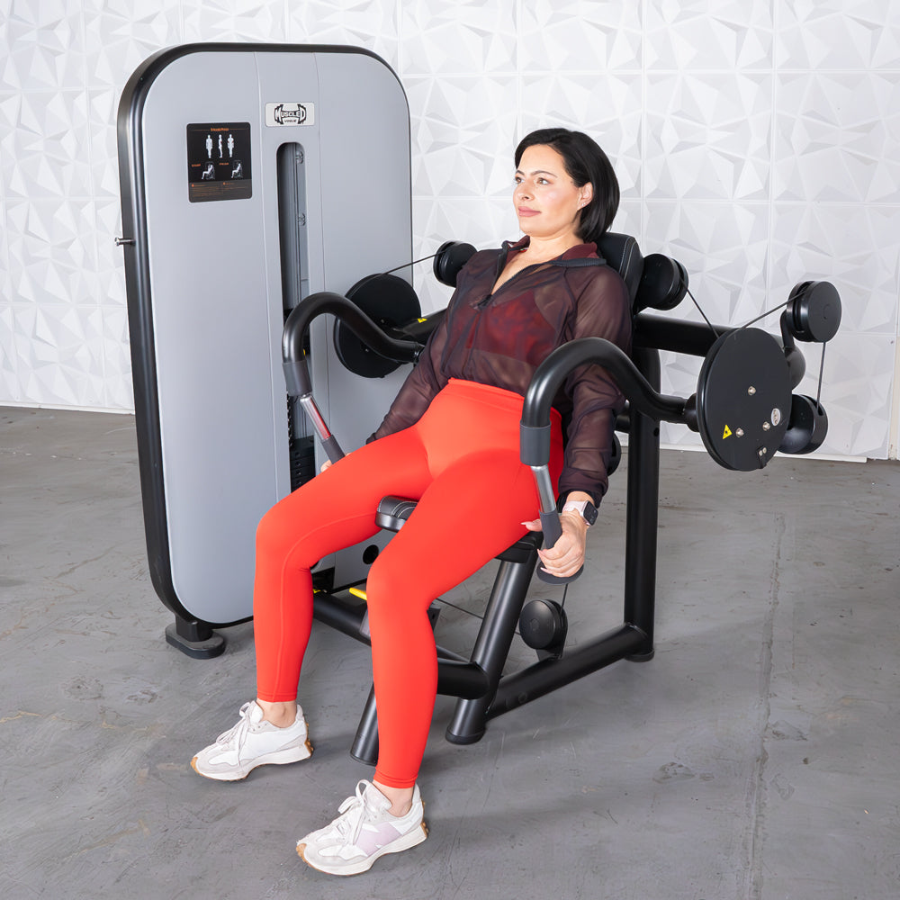 Woman using a seated triceps extension gym machine in a modern gym.