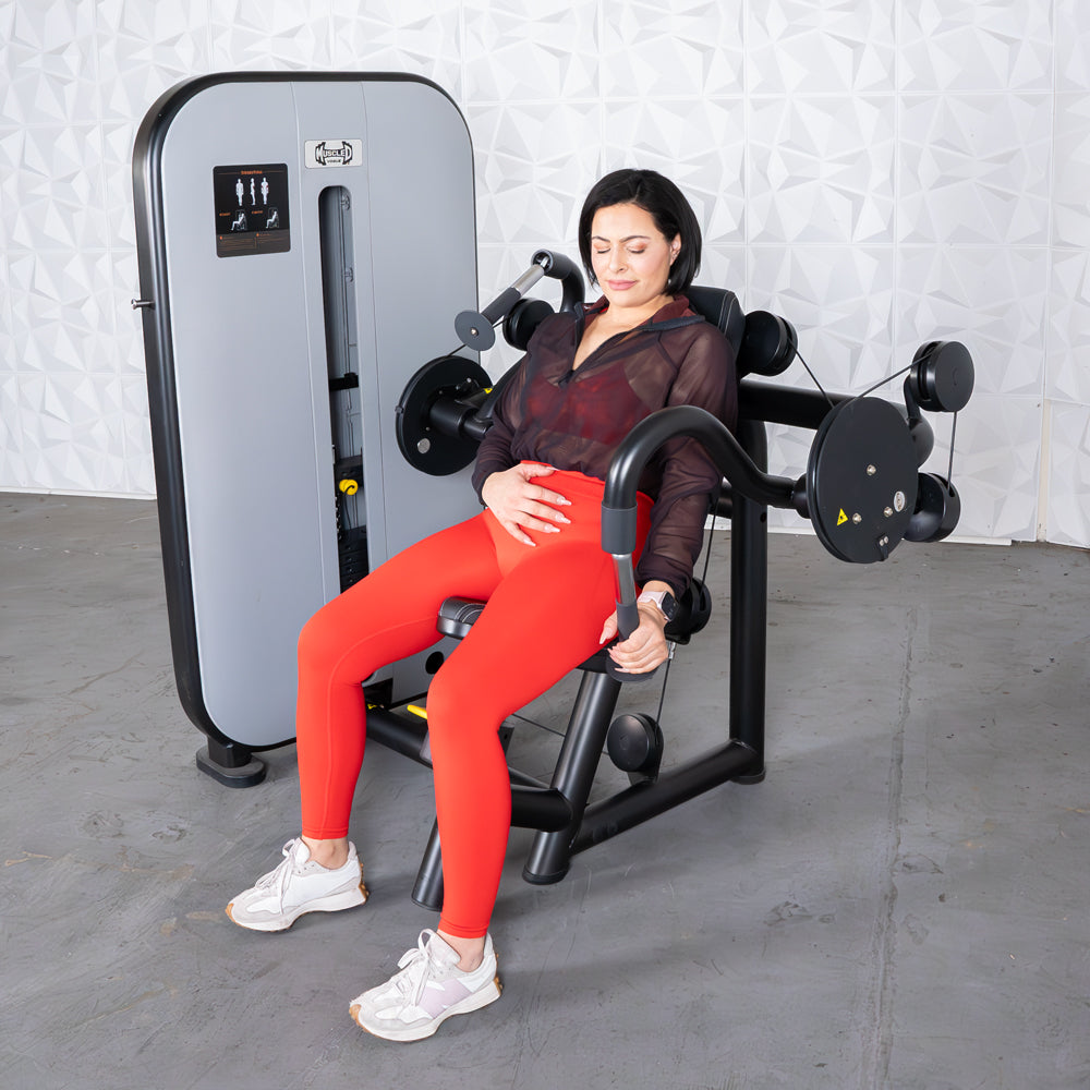 Woman in red leggings uses a triceps extension machine at the gym.